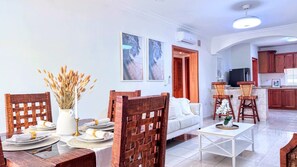 Ein modernes Wohnzimmer mit Essbereich, weißen Sofas, Holzstühlen und einer Küche im Hintergrund.