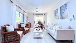 A spacious living room with a sofa, two wooden chairs, a dining table with chairs, and a ceiling fan. - Walk 2 Beach, Culture, Fun, Shops, Dine, Nightlife (Punta Cana)