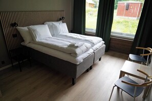 Una cama individual con cabecera, una mesita de noche, una silla y una ventana con cortinas.