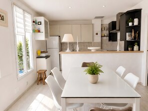 Een moderne keuken met witte kasten, een centraal eiland met een lamp, en een zithoek met een tafel en stoelen.