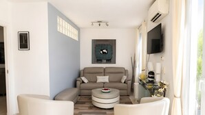 Uma sala de estar moderna com um sofá, duas poltronas, uma mesa de centro e uma televisão de tela plana na parede.