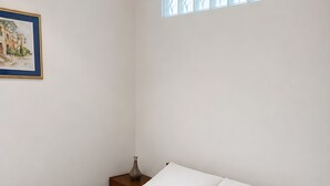 Um quarto modesto com uma cama, uma mesinha de cabeceira, um vaso e um quadro pendurado na parede.