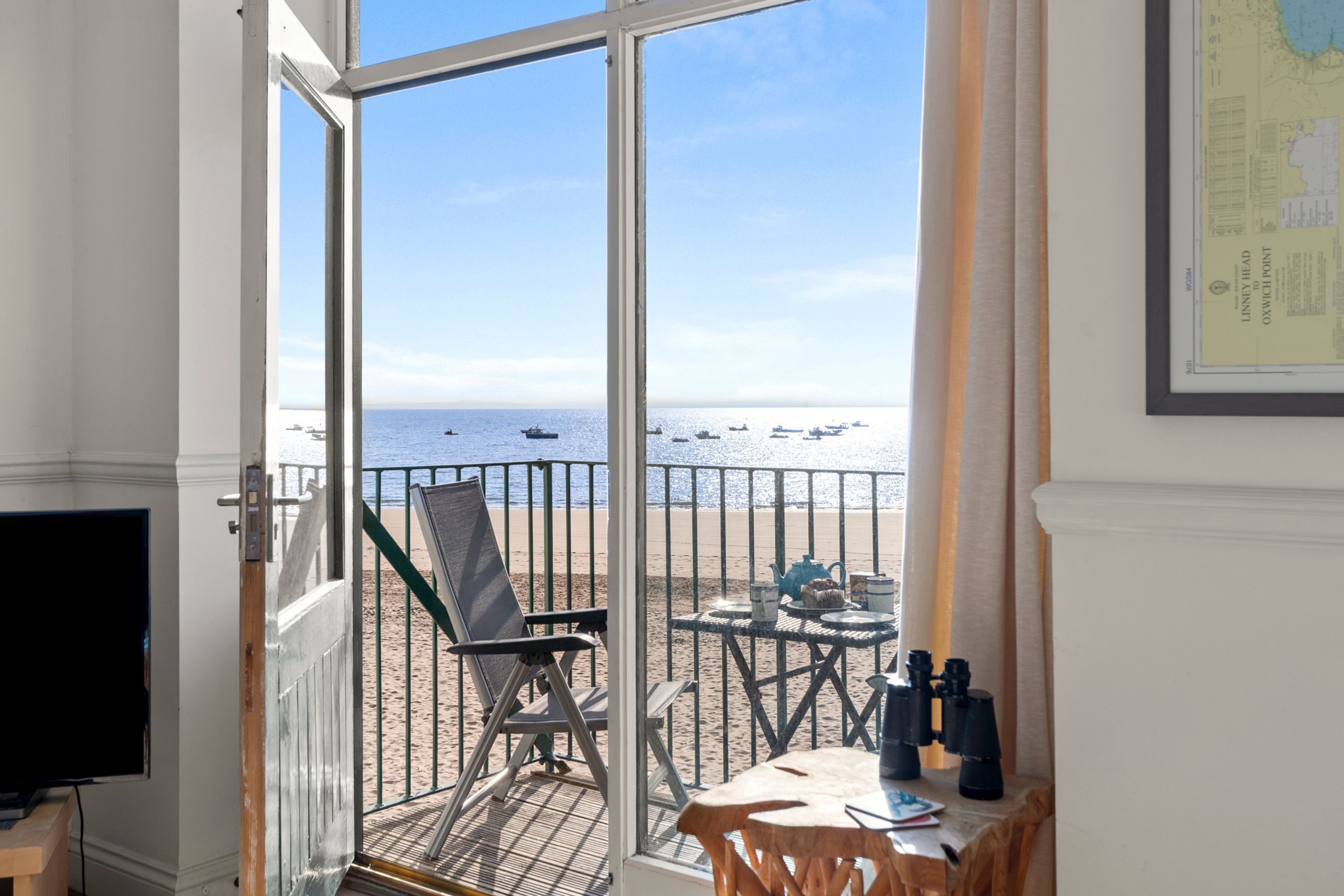 A room with a view of the sea, a table with a telescope, and a chair.