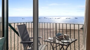 En strandutsikt med ett bord och stolar, ett räcke och båtar i vattnet.