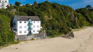 En vit byggnad med en grön balkong, belägen på en sandstrand med en skogbeklädd sluttning i bakgrunden.