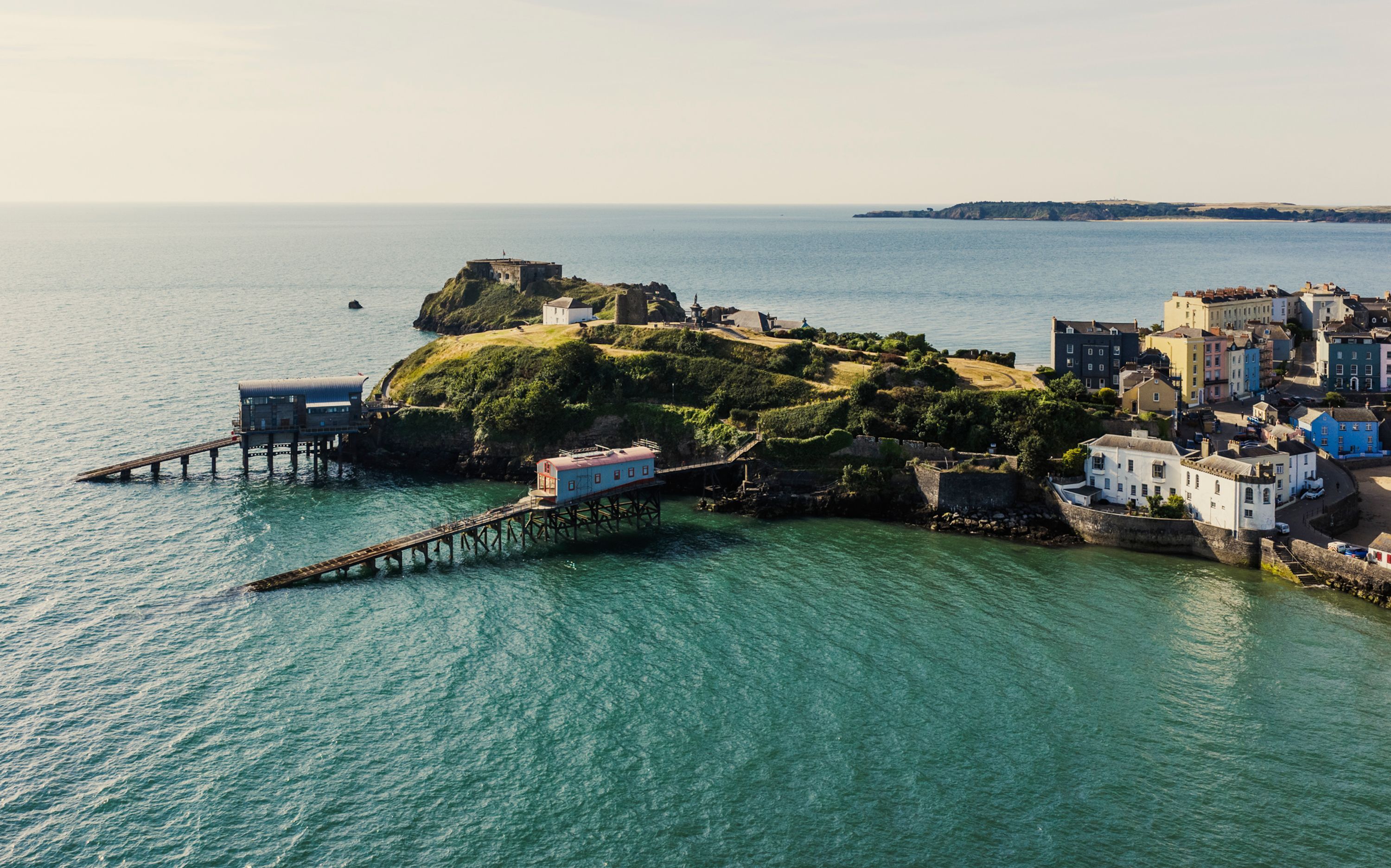 A coastal town with a prominent fort on a hill, a pier extending into the water, and a cluster of buildings along the shore.