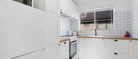 A modern kitchen with white cabinetry, a built-in oven, and a window overlooking a brick house.