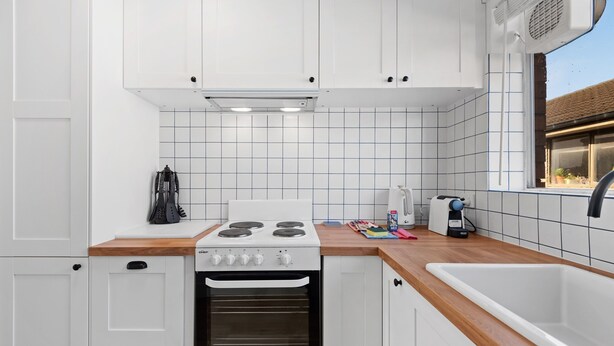 A modern kitchen with white cabinets, a built-in oven, a stove, and a window with a view of the outside. - Bright 1-bed Retreat in Kingsville (Melbourne)