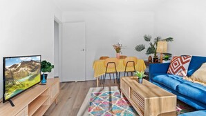 A living room with a TV, a sofa, a coffee table, a dining table with chairs, and a colorful rug. - Bright 1-bed Retreat in Kingsville (Melbourne)