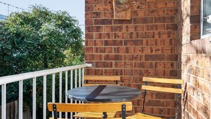 A balcony with a brick wall, a small table, and two chairs. - Bright 1-bed Retreat in Kingsville (Melbourne)