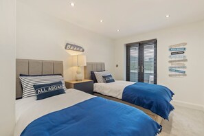 Un dormitorio con dos camas, una mesita de noche, una lámpara y una pared decorada con motivos náuticos.