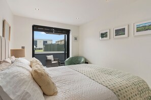 A bedroom with a large bed, a green chair, a window, and three framed pictures on the wall.