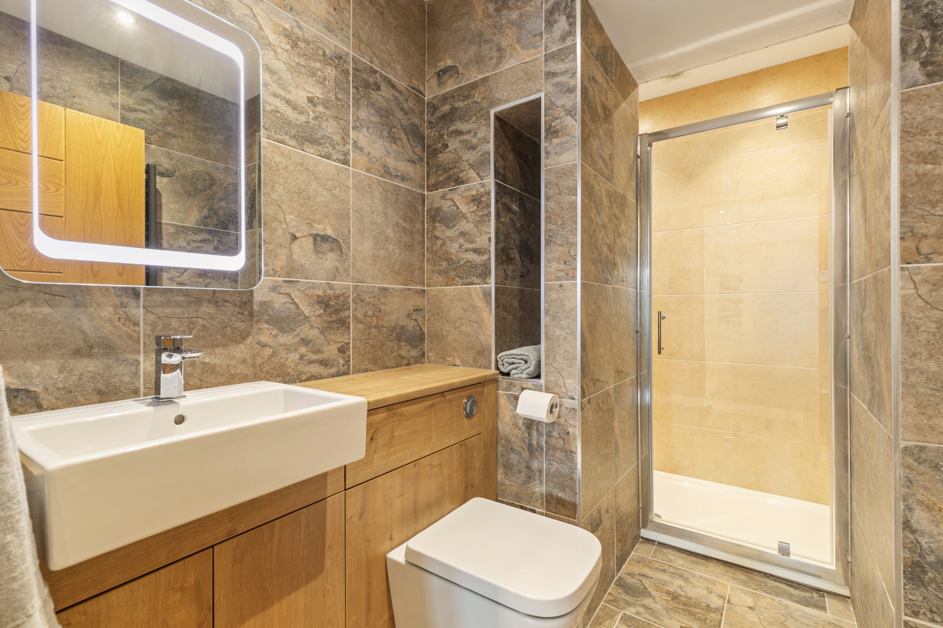 Een badkamer met een witte wastafel, houten opbergmeubel, een spiegel, douchecabine en toilet.