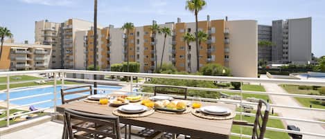 A balcony with a table set for breakfast, overlooking a swimming pool and a residential area with palm trees.