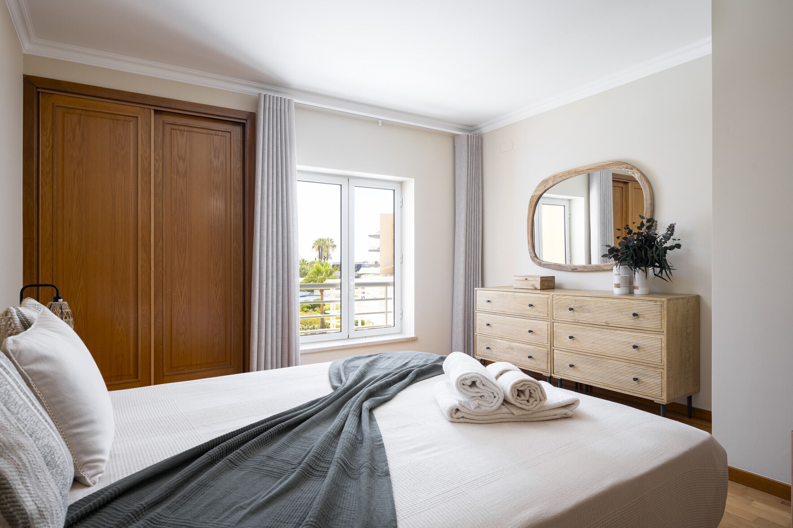 Ein Hotelzimmer mit einem großen Bett, einem Holzschrank, einem Schminktisch und einem Fenster mit Blick auf einen Balkon.