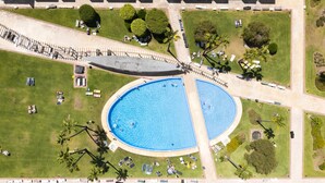 En vy över en park från ovan, med en stor ovalformad pool omgiven av gräs, träd och en promenadstig.