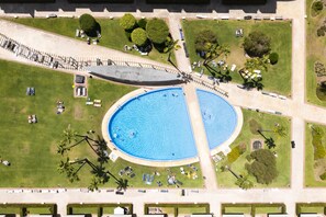Eine Luftaufnahme eines Parks mit einem großen, ovalen Pool, umgeben von Rasenflächen, Bäumen und einem Fußweg.