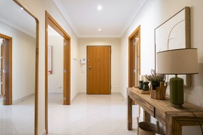 A hallway with a wooden door, a console table with a lamp, and a potted plant. - Moura Praia by Hdproperties (Vilamoura)