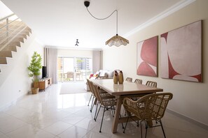 A spacious dining area with a high ceiling, a staircase on the left, and a view of the outdoors through a glass door. - Moura Praia by Hdproperties (Vilamoura)