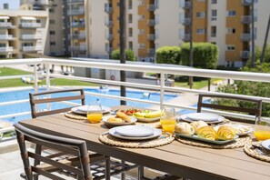 A dining table set with breakfast items, a pool in the background, and a view of apartment buildings. - Moura Praia by Hdproperties (Vilamoura)