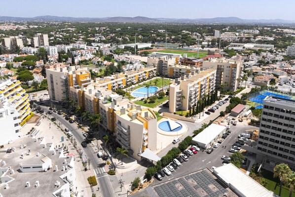 A high-rise residential building with multiple balconies, a central courtyard with a pool, and a view of the surrounding cityscape. - Moura Praia by Hdproperties (Vilamoura)