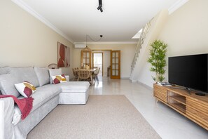 Ein modernes Wohnzimmer mit Sofa, Couchtisch, TV-Möbel und einem Essbereich mit Tisch und Stühlen.