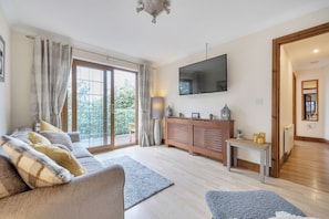 A modern living room with a sofa, a flat-screen TV, and a wooden cabinet. - 2-bed - Sleeps 4 - Parking & Ev Charging (Wadebridge)