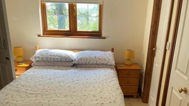 A bedroom with a bed, a window, a nightstand, a dresser, and a door. - 2-bed - Sleeps 4 - Free Parking & Ev Charging (Wadebridge)