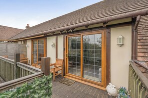 A covered outdoor seating area with wooden furniture and a glass door entrance. - 2-bed - Sleeps 4 - Parking & Ev Charging (Wadebridge)
