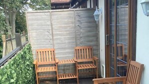 A patio with wooden furniture including a table and chairs, a small rug, and a metal fence. - 2-bed - Sleeps 4 - Free Parking & Ev Charging (Wadebridge)