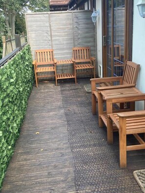 A patio with wooden furniture including a table and chairs, a small rug, and a metal fence. - 2-bed - Sleeps 4 - Free Parking & Ev Charging (Wadebridge)