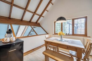 Uma sala de jantar com mesa de madeira, cadeiras, um banco, uma máquina de café e um vaso com flores.
