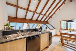 Una cocina con techo de madera, un lavamanos, lavavajillas y comedor con mesa y sillas.