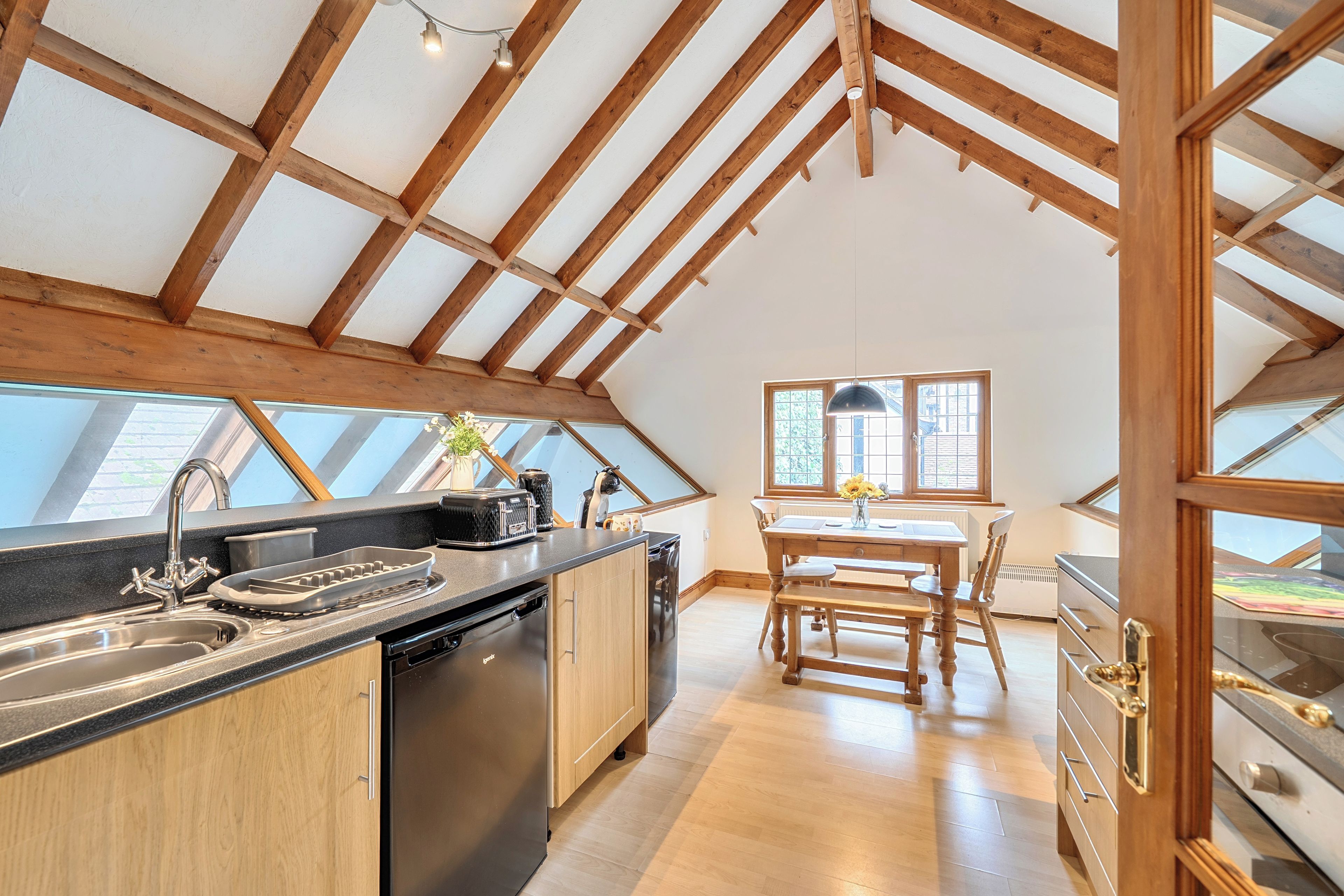 A kitchen with a wooden ceiling, a dining area with a table and chairs, and a view through a window.