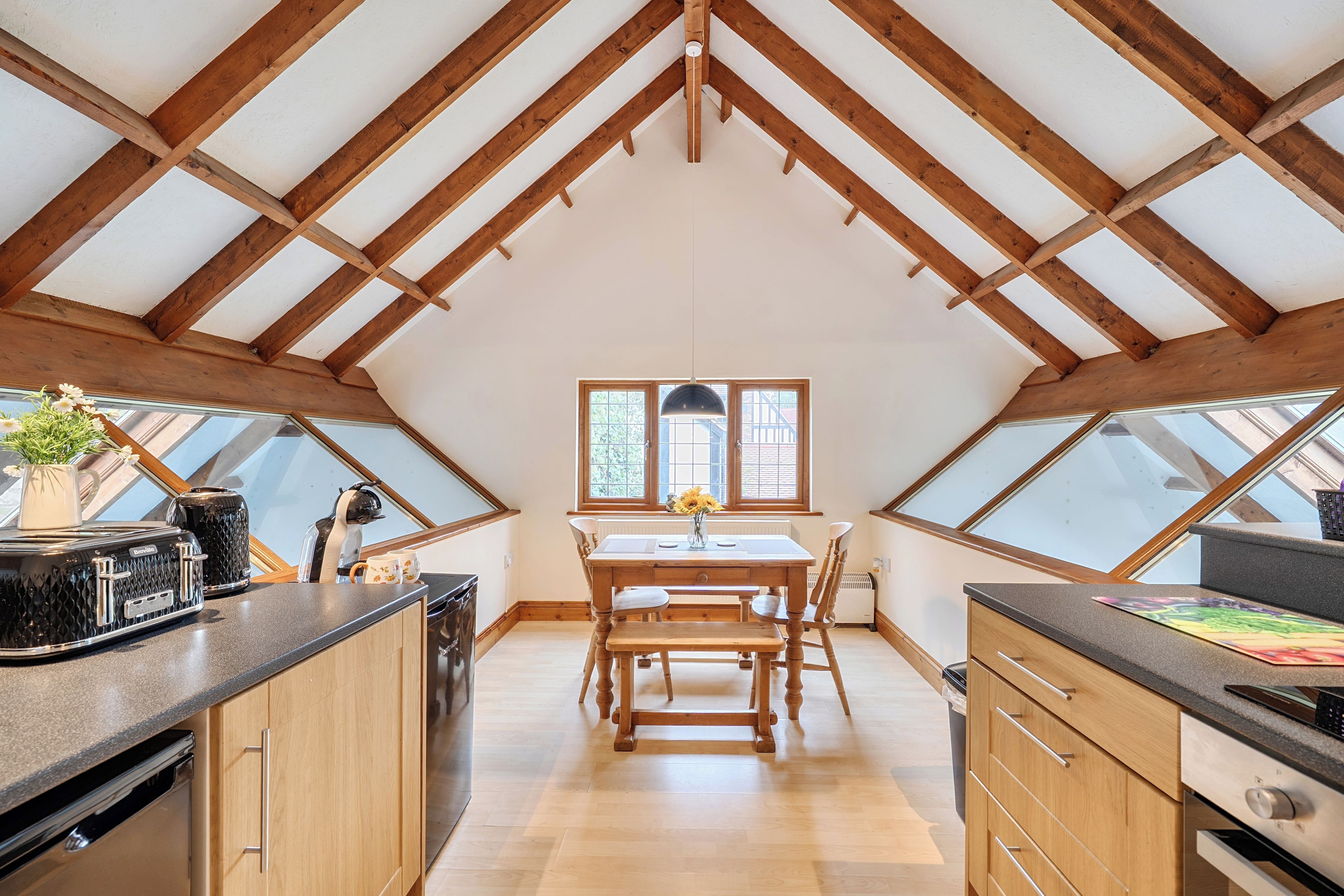 A kitchen with a wooden table, two windows, and a skylight.