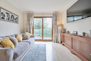 Una sala de estar moderna con un sofá gris, un mueble de madera y un amplio ventanal con cortinas.