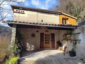 A two-story building with a tiled roof, a wooden door, and a small porch area with potted plants. - A vacation rental for 10 people, perfect for swimming, biking, and rock climbing. Pets are allowed. (Saint-Maurice-en-Chalencon)