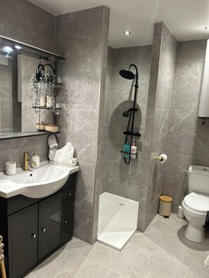 A modern bathroom with a white sink, black cabinets, a glass shower enclosure, and a toilet. - Le Petit Rocher Doré: a unique getaway with a view of the Rock. (Pierrelatte)