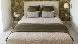 A bedroom with a bed, a headboard, a wall with a leaf pattern, a floor lamp, and a bedside table. - Le Petit Rocher Doré: a unique getaway with a view of the Rock. (Pierrelatte)