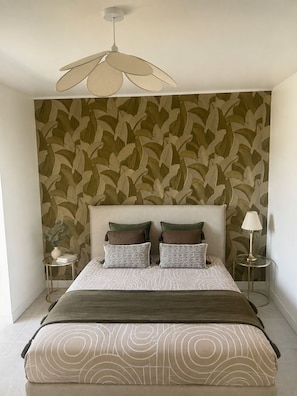 Ein Schlafzimmer mit einem Bett, einem Kopfteil, einer Wand mit Blättermuster, einer Stehlampe und einem Nachttisch.