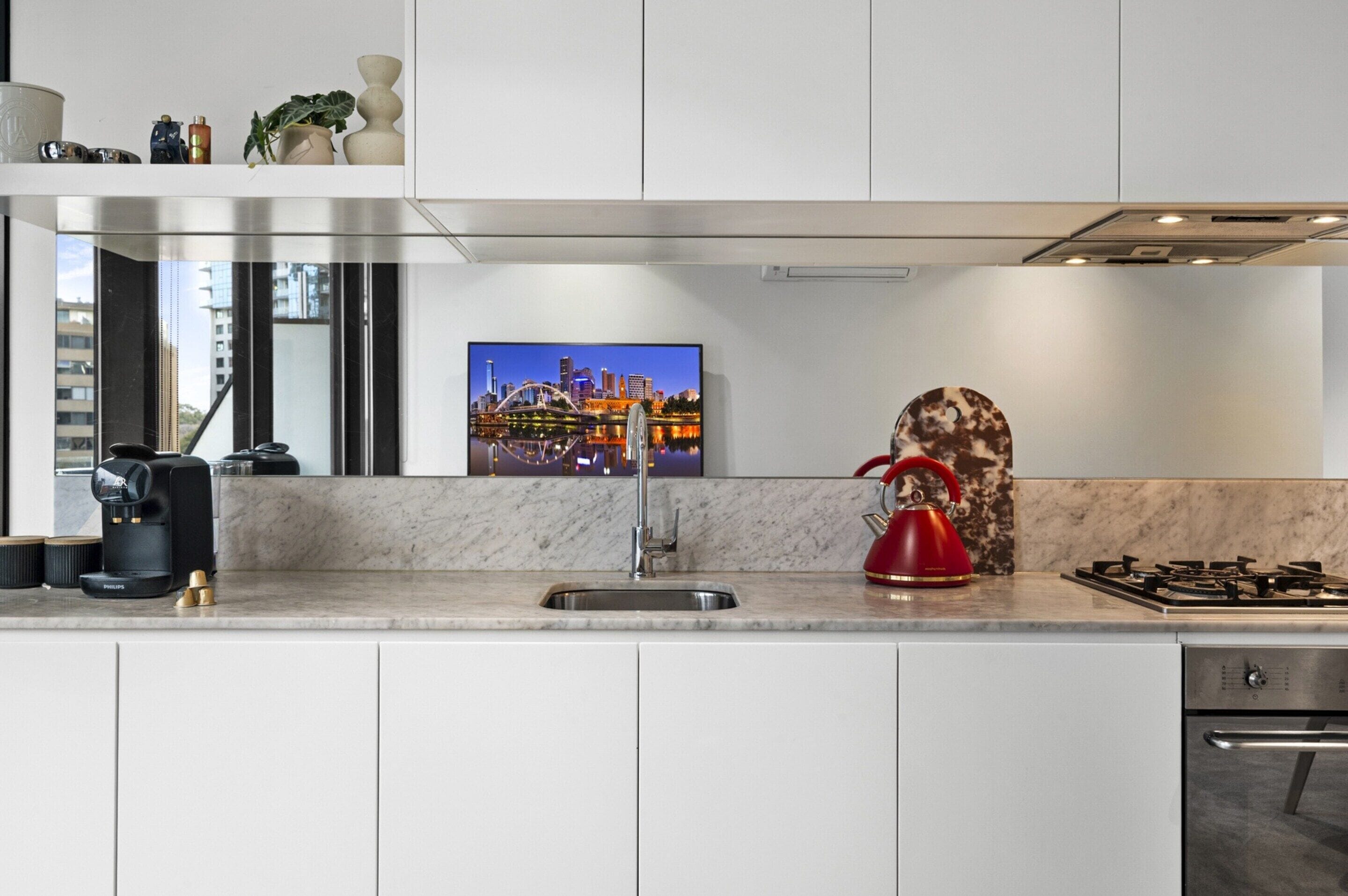 A modern kitchen with a built-in stove, a coffee maker, and a red kettle.
