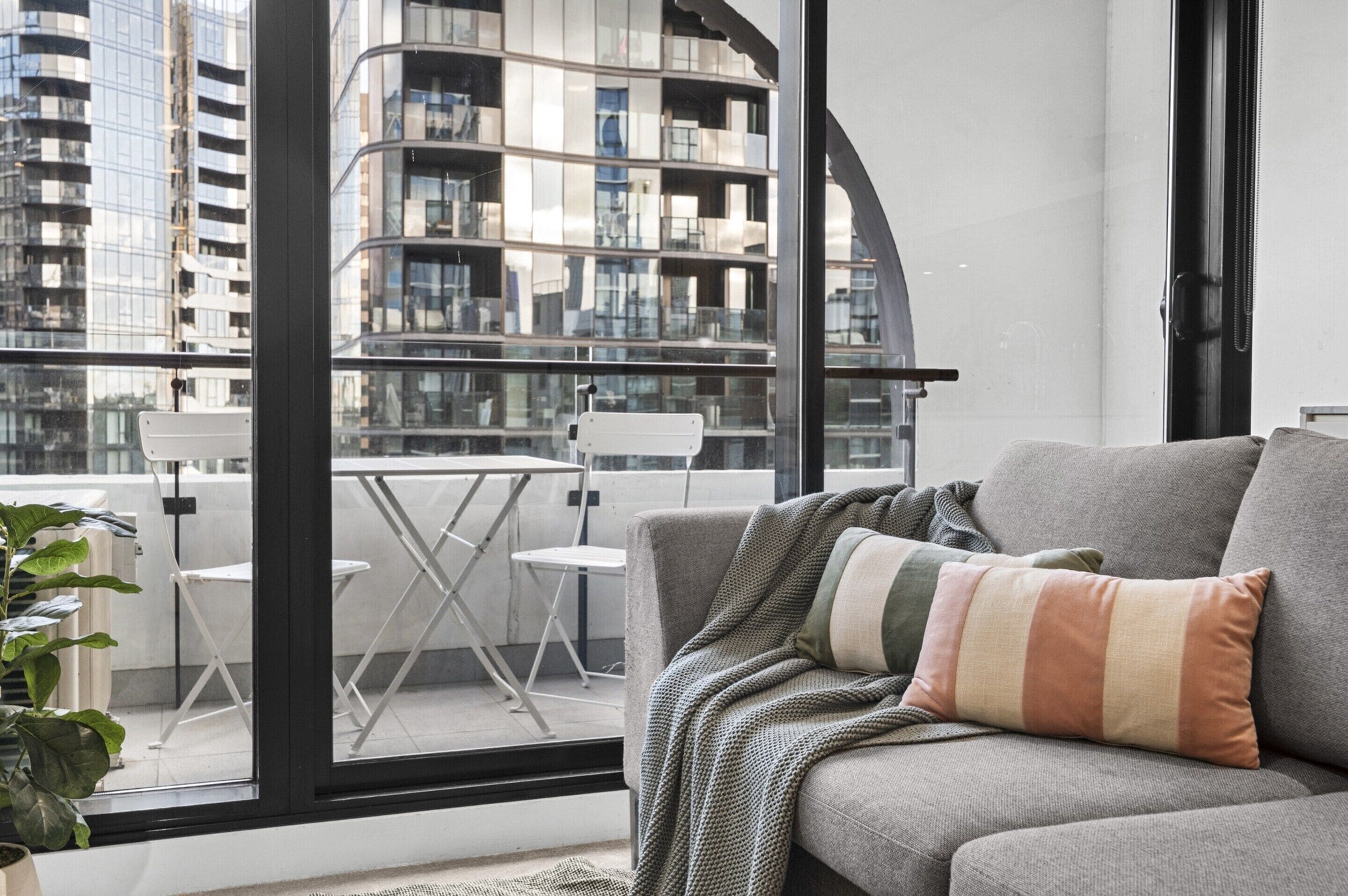 A modern living room with a grey sofa, a striped throw pillow, and a view of a cityscape through large windows.