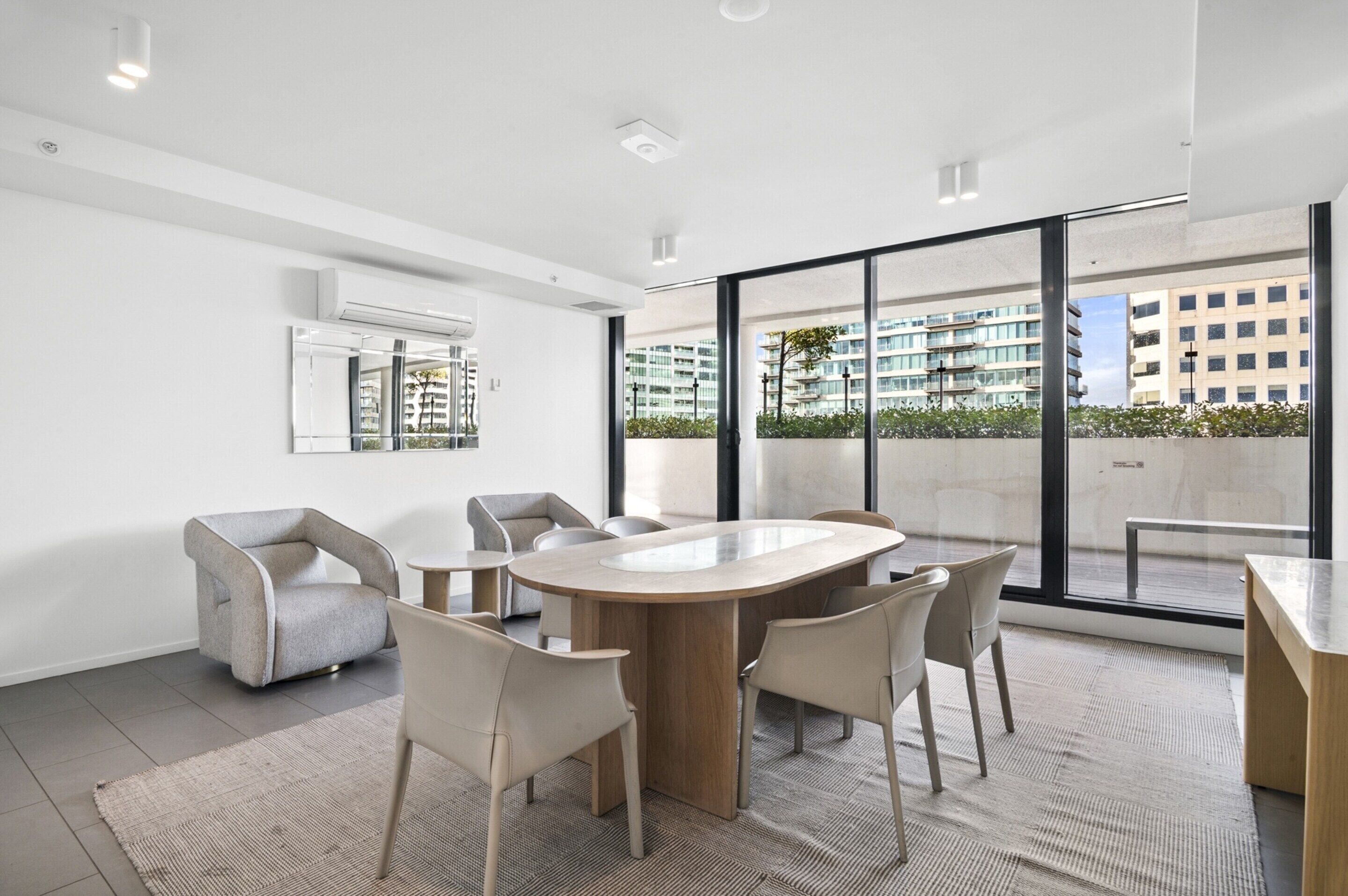 A modern meeting room with a large oval table, comfortable chairs, and large windows offering a view of a cityscape.