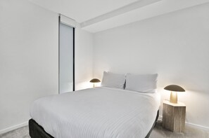 Ein schlicht eingerichtetes Schlafzimmer mit einem Bett, zwei Nachttischlampen und einer Schiebetür.