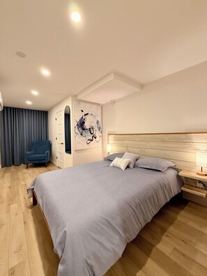 Ein modernes Schlafzimmer mit einem großen Bett, einem blauen Sessel und einem an der Wand befestigten Kunstwerk.