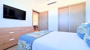 A bedroom with a bed, a TV mounted on the wall, a wardrobe, and a desk with a chair. - The Beach Crystal Lagoon View Downtown Punta Cana (Punta Cana)