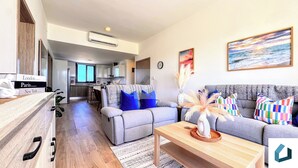 Ein modernes Wohnzimmer mit einem grauen Sofa, einem Holztisch und einer Küche im Hintergrund.
