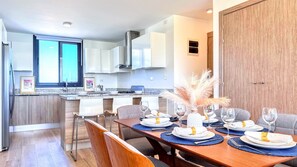 A modern kitchen with white cabinets, a stainless steel range hood, and a dining area with a wooden table set for four. - The Beach Crystal Lagoon View Downtown Punta Cana (Punta Cana)