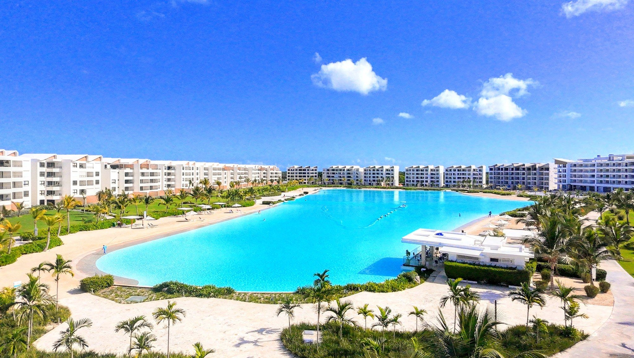 A resort with a large swimming pool, multiple hotel buildings, and palm trees.