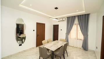 A dining room with a marble table and chairs, a wooden door, and a large window with curtains.